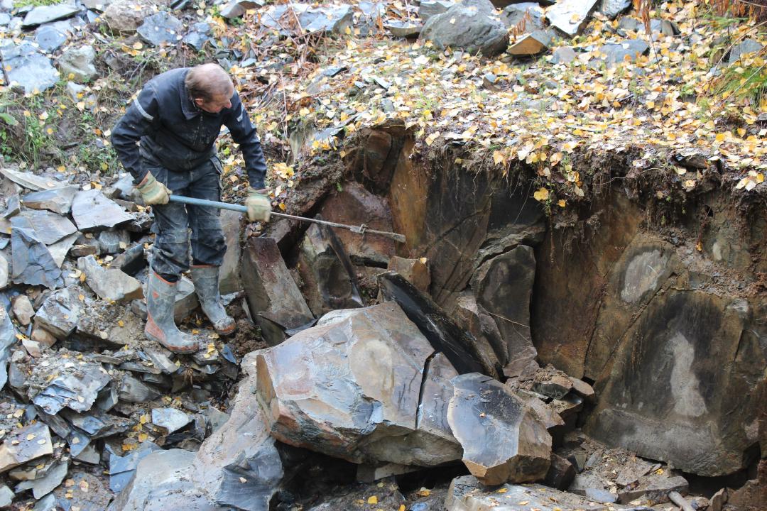 Dick Persson omgiven av stenbitar bryter lerskiffer i skogsmiljö